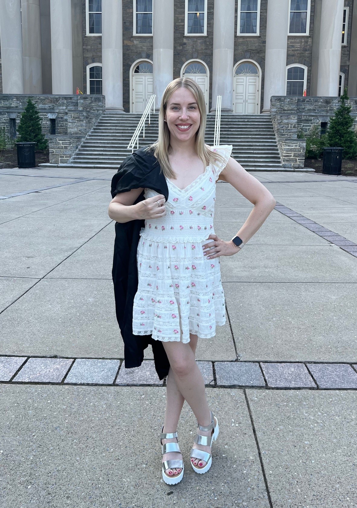 Halley Maxin stands with her graduation gown. Halley is in a white dress and shoes.